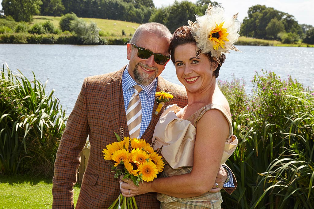 Bride and groom outside lake with yellow sunflowers