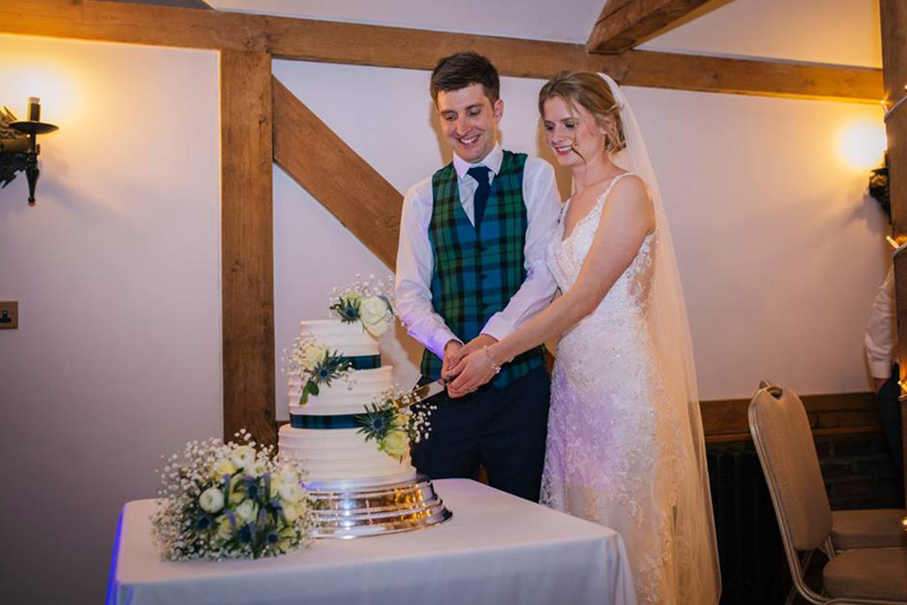 The happy newlyweds cut their three-tiered wedding cake decorated in white roses and a deep blue ribbon