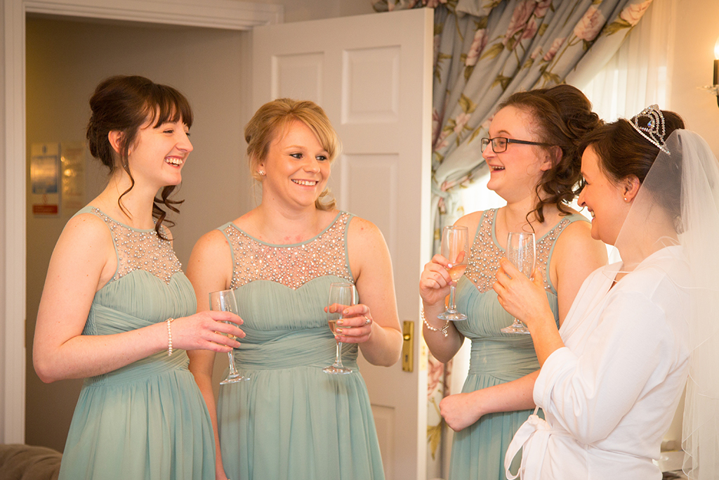 The bride and her bridesmaids in their pastel blue dresses enjoy a toast while the bride prepares to be married