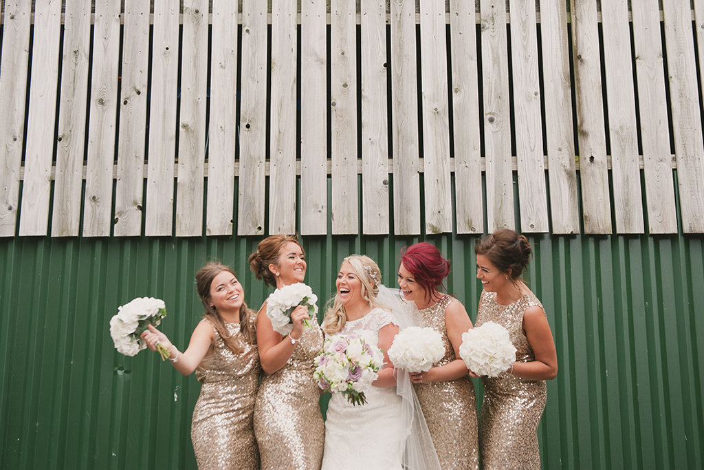 The bride laughs with her bridesmaids who each wore long gold sparkly bridesmaid dresses