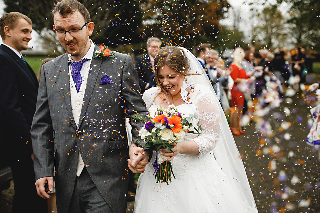 Guests throw colourful natural confetti over the newlyweds at this barn wedding in Cheshire