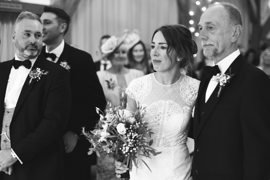 The groom takes a glance at his beautiful wife to be at the wedding ceremony at Sandhole Oak Barn in Cheshire