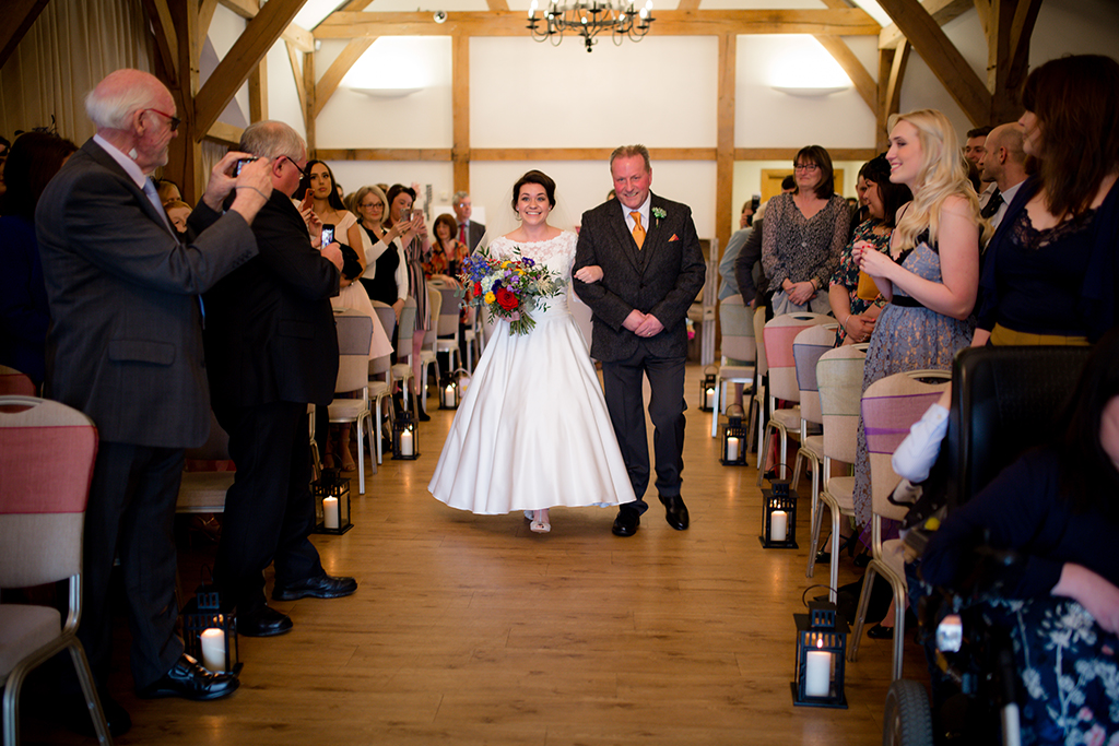 The bride walks down the aisle with her father before the wedding ceremony at Sandhole Oak Barn