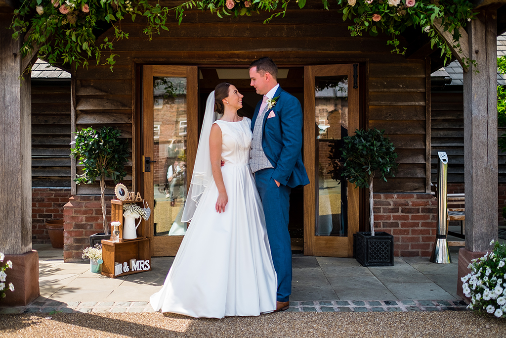 The bride and groom pose for a photo at the entrance to the oak barn at Sandhole Oak Barn
