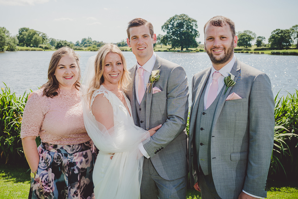 The bride and groom pose for a photo with their bridesmaid and best man at this waterside wedding venue 