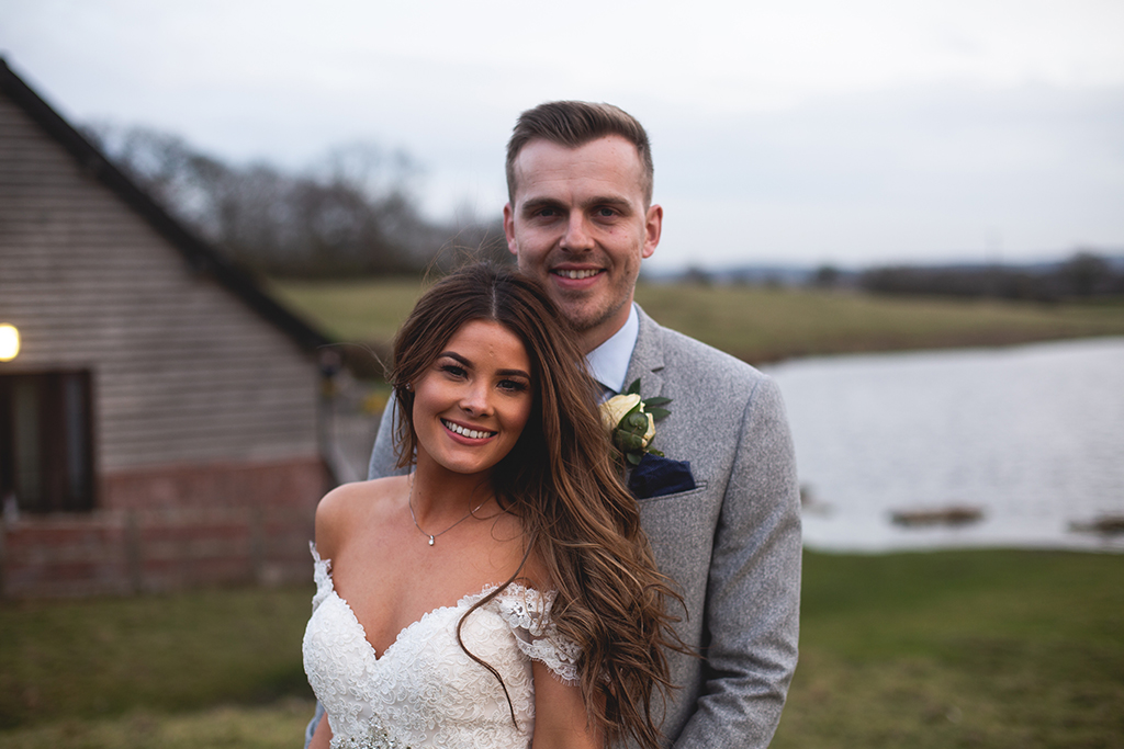 The bride and groom have their photo taken with the lake as their backdrop at this rural wedding venue in Cheshire