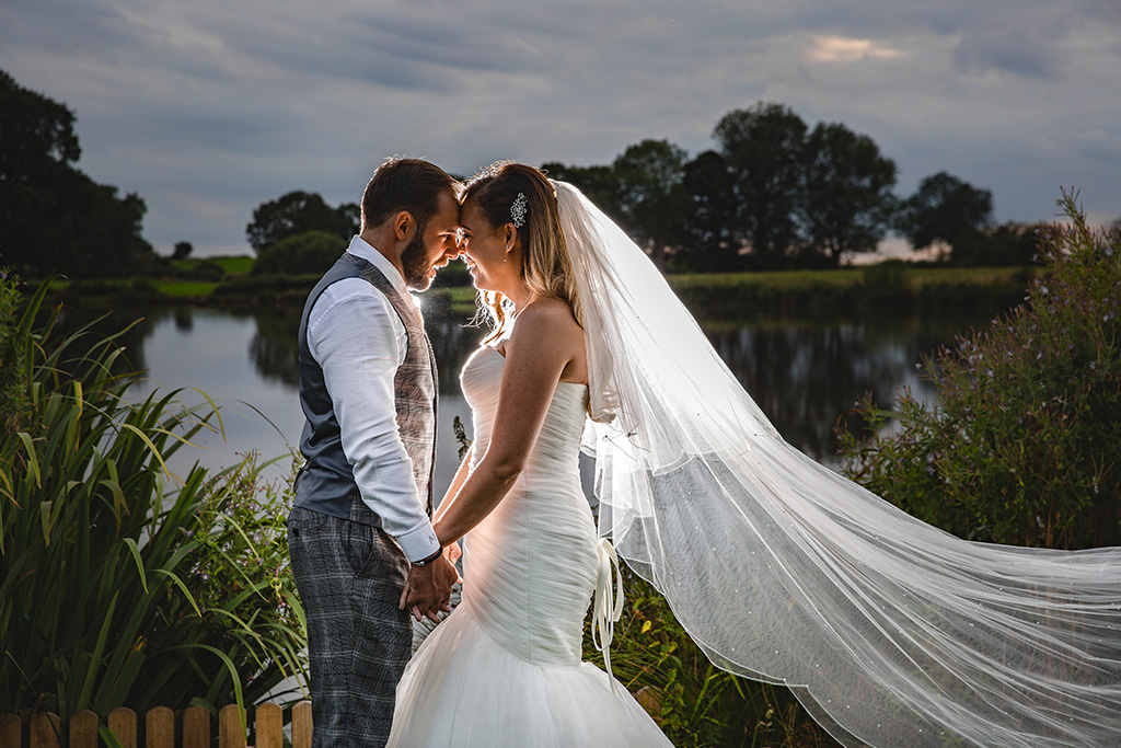 The bride and groom have their photo taken in front of the lake at Sandhole Oak Barn in the North West