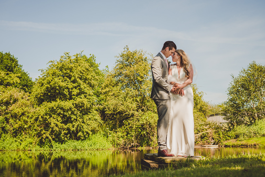 The bride and groom pose for a photo at the waterside of this barn wedding venue