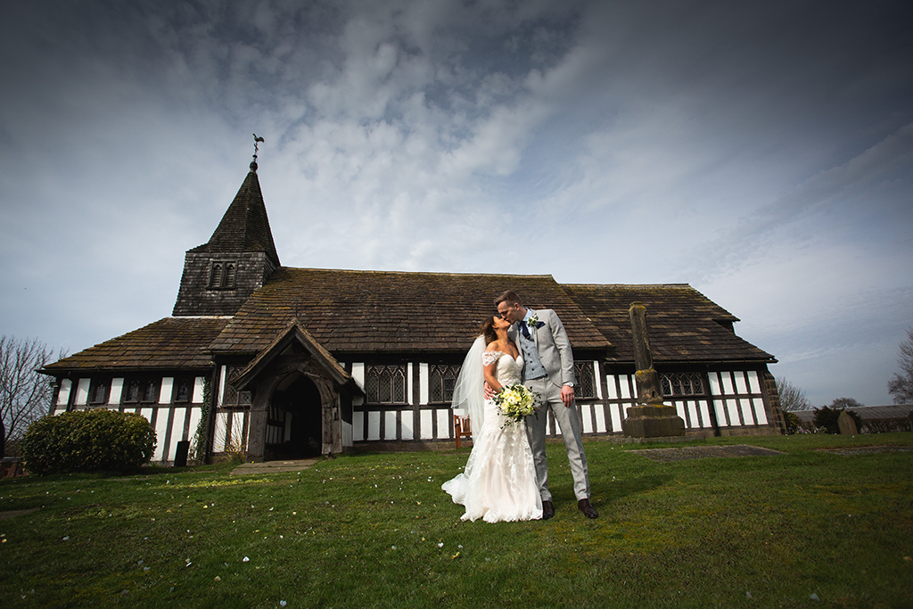 The bride and groom pose for a wedding photo in front of St Paul’s church at this barn wedding in Cheshire