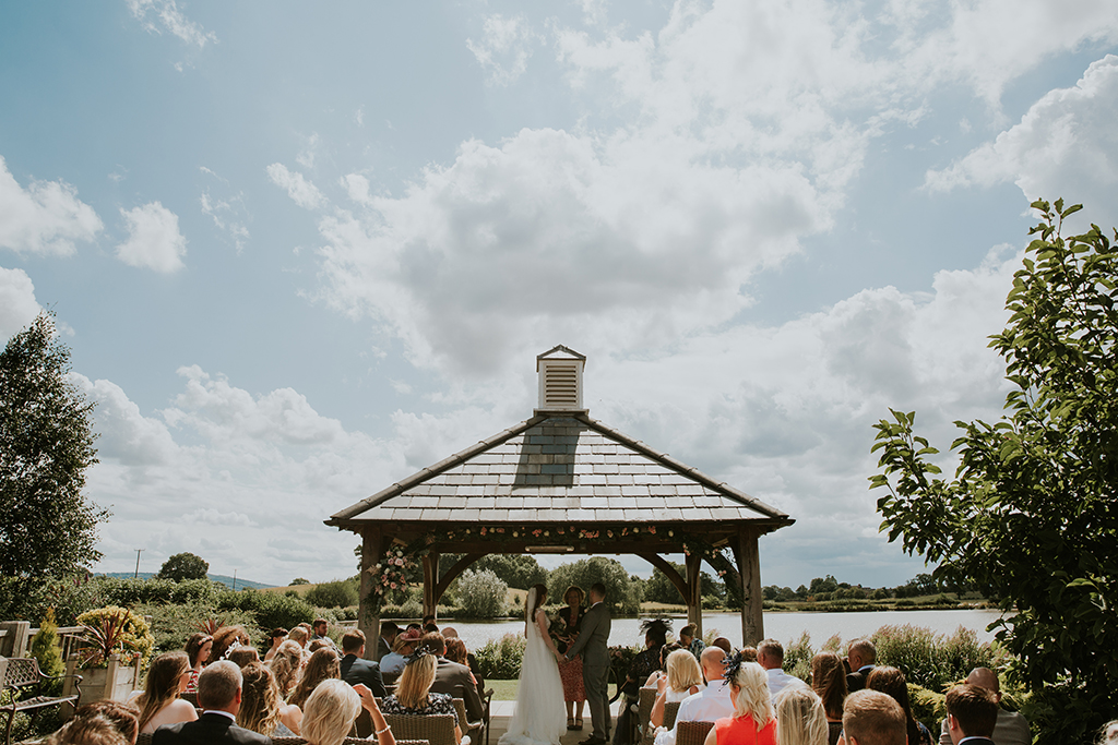 The bride and groom say their vows under the Clock Tower on a beautifully sunny day at this barn wedding venue in Cheshire