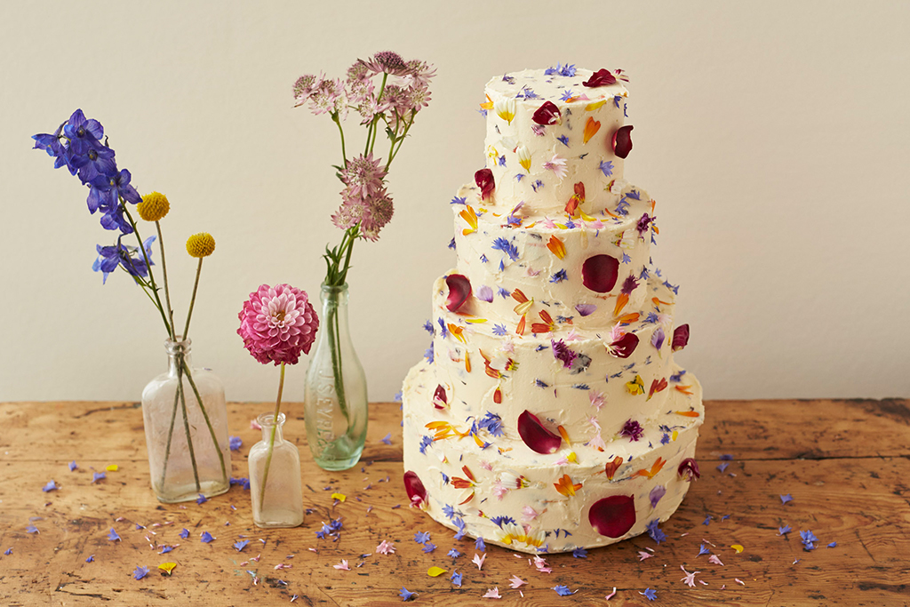 This three-tier wedding cake has been iced with butter cream and decorated with edible flowers