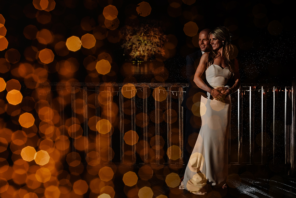 The happy newlyweds pose for a creative evening wedding photo with twinkly fairy lights in shot at Sandhole Oak Barn