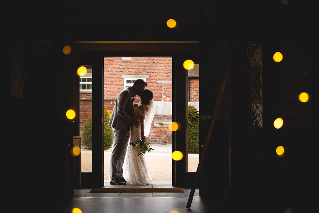 The bride and groom pose for a wedding photo in the doorway of the Oak Barn at Sandhole Oak Barn an exclusive wedding venue in Cheshire