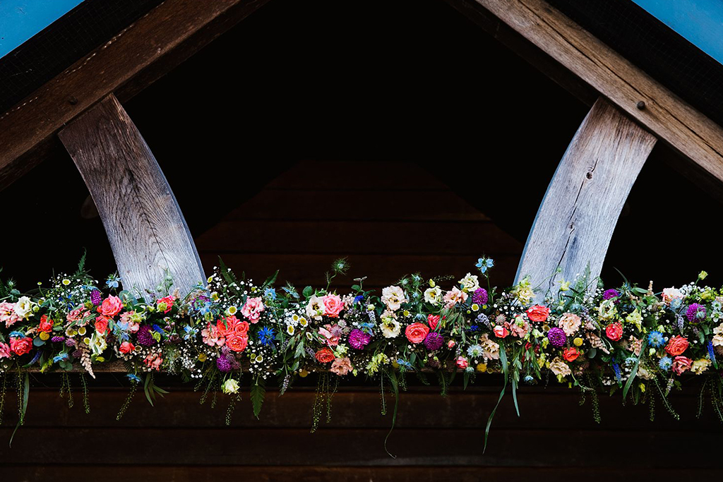 The doorway to the barn was decorated with a beautiful colourful summer flower garland at this barn wedding near Manchester