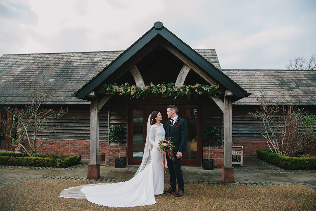 The stunning bride and her groom pose for a photo at the entrance to this rustic barn venue in Cheshire