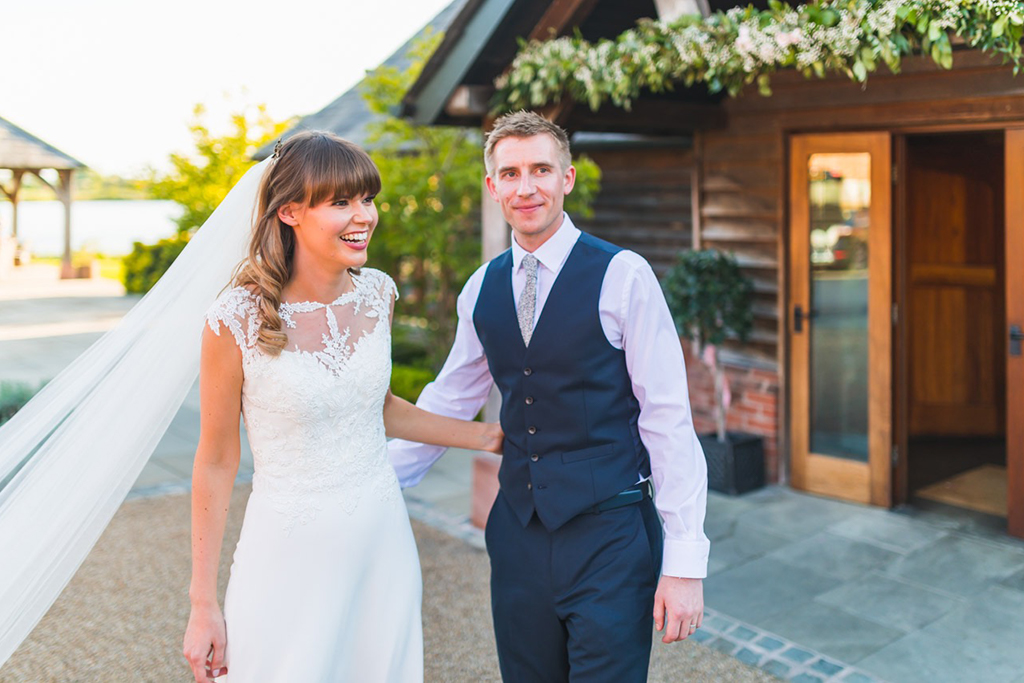 The bride wears an elegant wedding dress with a lace top and the groom wears a navy 3-piece wedding suit at Sandhole Oak Barn