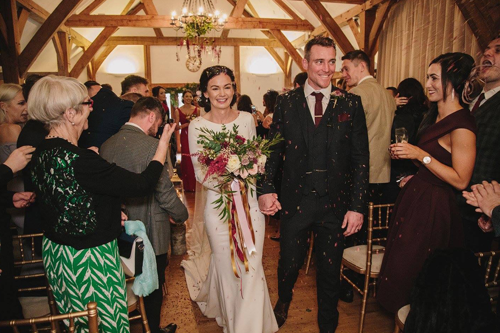 The bride and groom have natural confetti thrown over them after their wedding ceremony at Sandhole Oak Barn in the North West