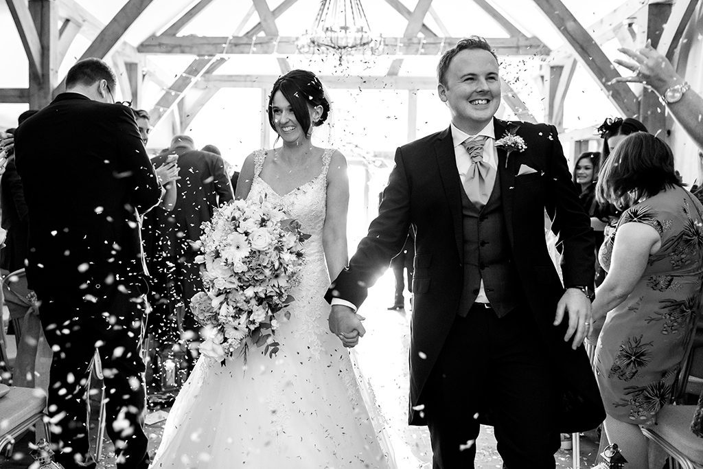 The happy newlyweds walk back down the aisle as their guests throw confetti at this wedding at Sandhole Oak Barn in the North West