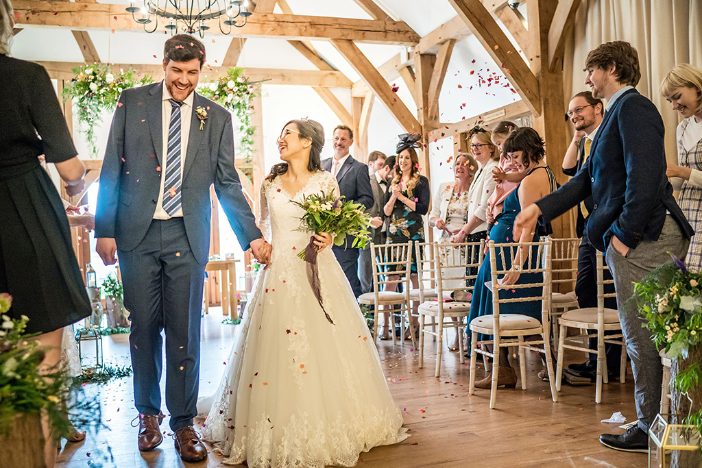 The happy newlyweds have confetti thrown over them as they walk back down the aisle as husband and wife at Sandhole Oak Barn