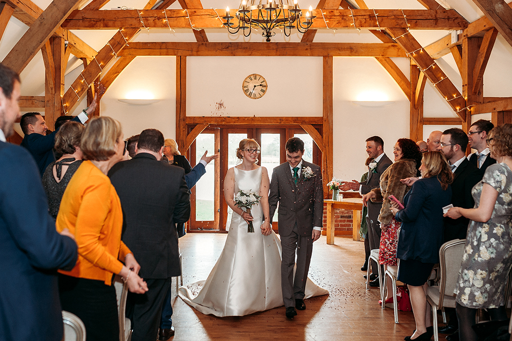 The happy newlyweds walk up the aisle as husband and wife as guests throw confetti at this barn wedding