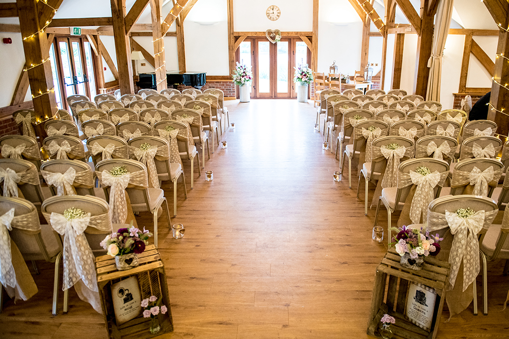 The Oak Barn looks beautiful set up for the wedding ceremony with the chairs decorated with pretty lace and hessian sashes