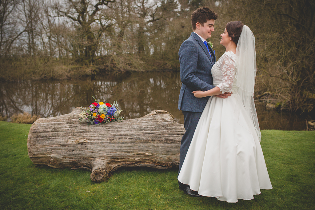 The happy newlyweds pose for a photo by the lake at this rural wedding venue in Cheshire
