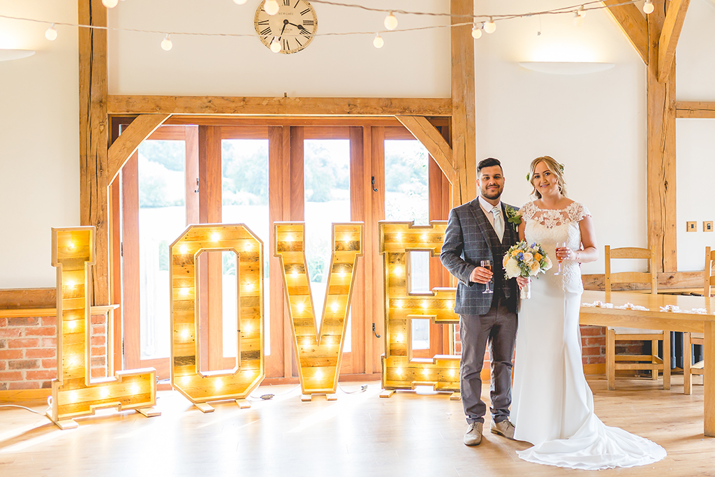 The happy newlyweds pose for a wedding photo by the love letter lights at this summer wedding at Sandhole Oak Barn