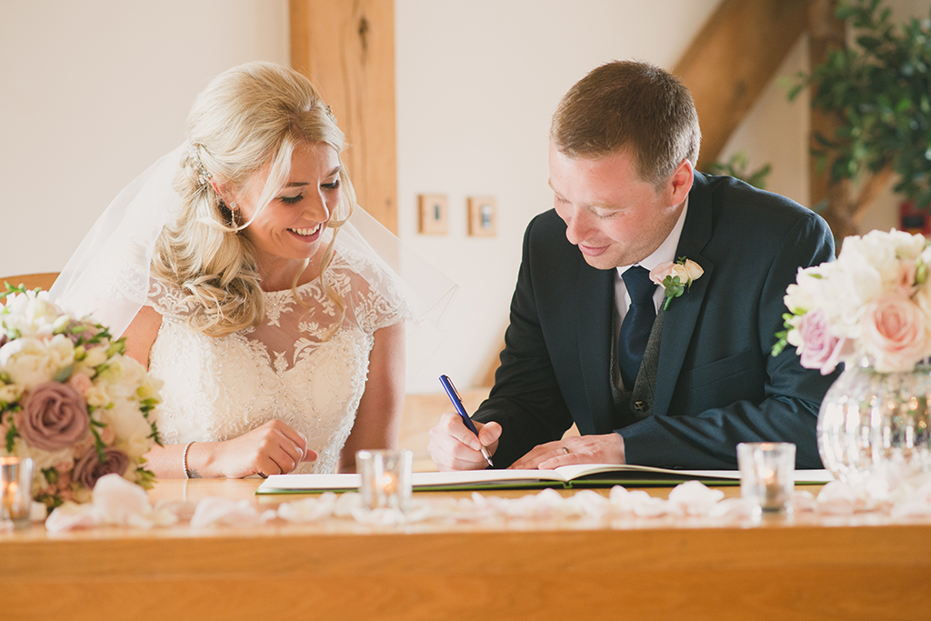 The happy newlyweds sign the register together inside the stunning barn wedding venue