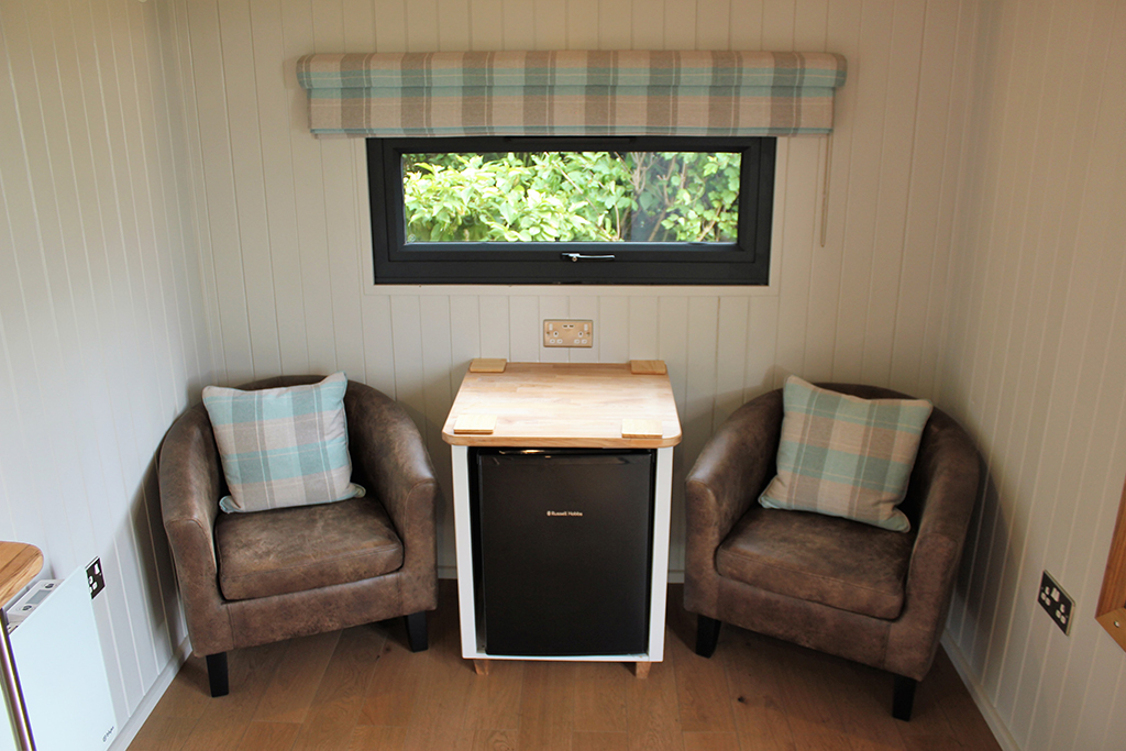 Comfy tub chairs and fridge in the shepherds hut partner preparation room at Sandhole Oak Barn