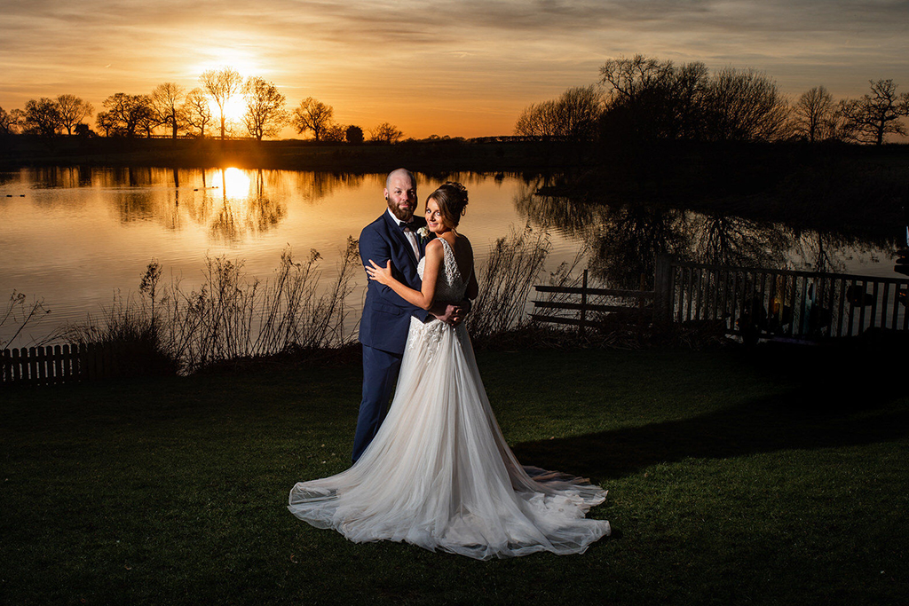 The happy couple pose for a wedding photo by the lake at their wedding evening