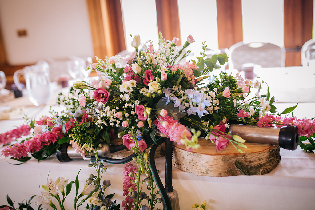 The top table was decorated with a beautiful arrangement of colourful spring flowers and dairy farming parts at Sandhole Oak Barn in Cheshire