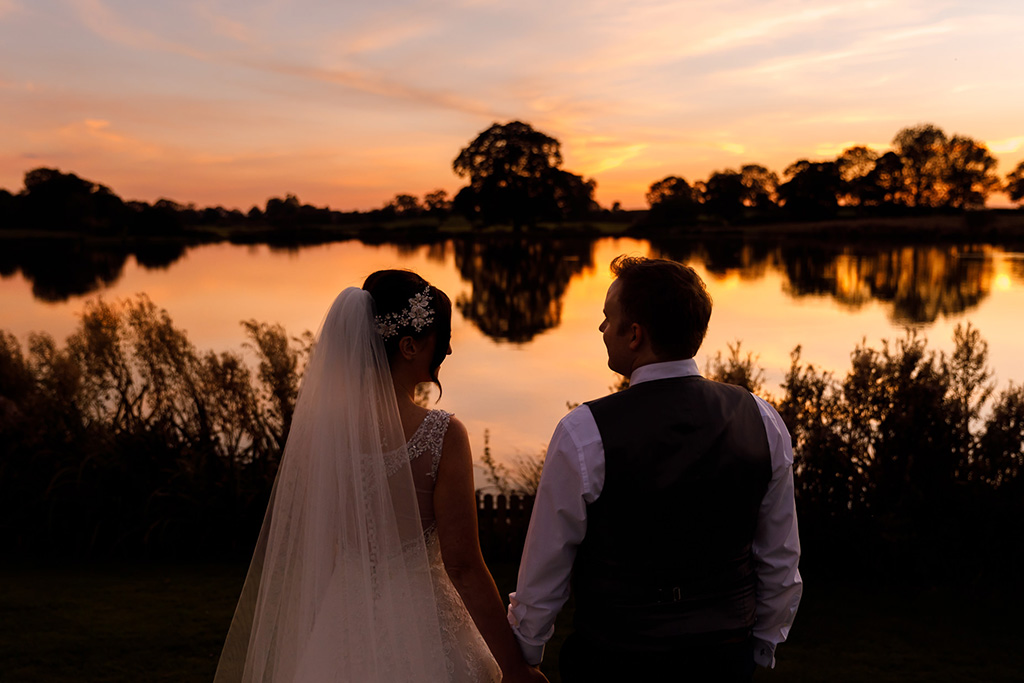 The happy newlyweds enjoy the views of the sun setting over the lake at this rural wedding venue in Cheshire