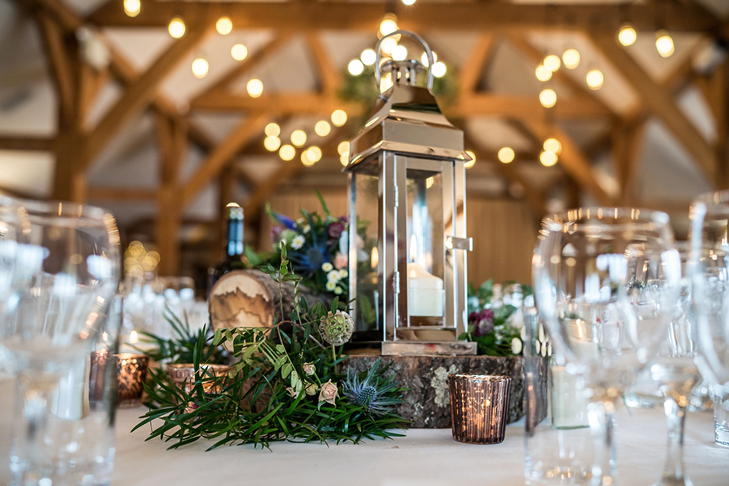The couple chose lanterns and seasonal flowers displayed on log slices as their table centrepieces at their barn wedding in Cheshire