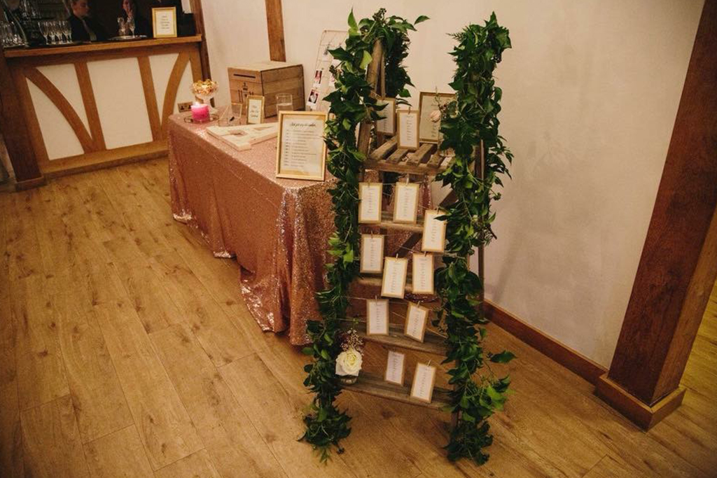 The couple chose a rustic wooden ladder shelf decorated with lush foliage to display their table plan at Sandhole Oak Barn
