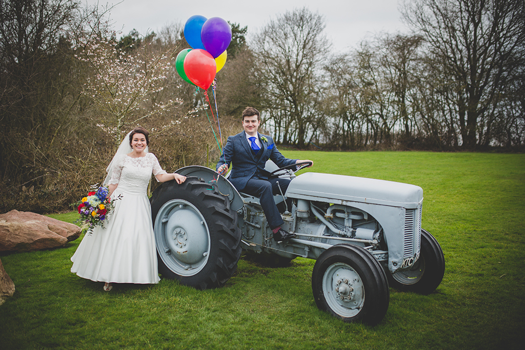 The happy newlyweds pose for a fun wedding photo on the tractor at Sandhole Oak Barn in Cheshire