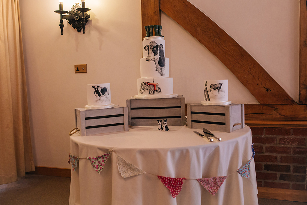 The couple chose a three tier wedding cake and two separate cakes all hand painted with farming designs at their rustic barn wedding