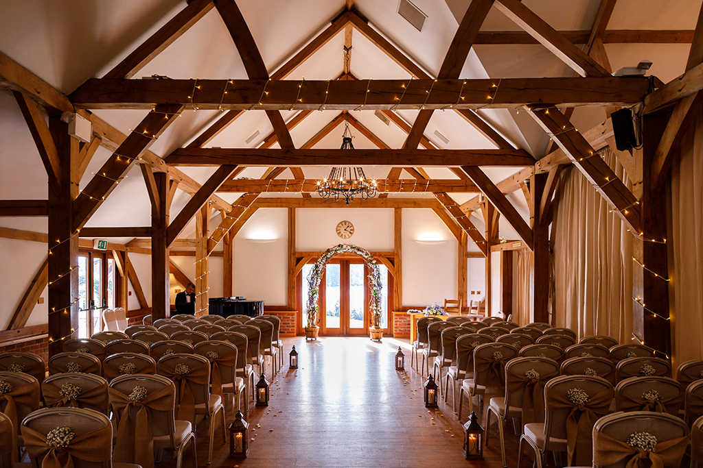 The rustic Oak Barn is set up for the wedding ceremony with fairy lights on the beams and pretty bunches of gypsophilia tied to chairs.