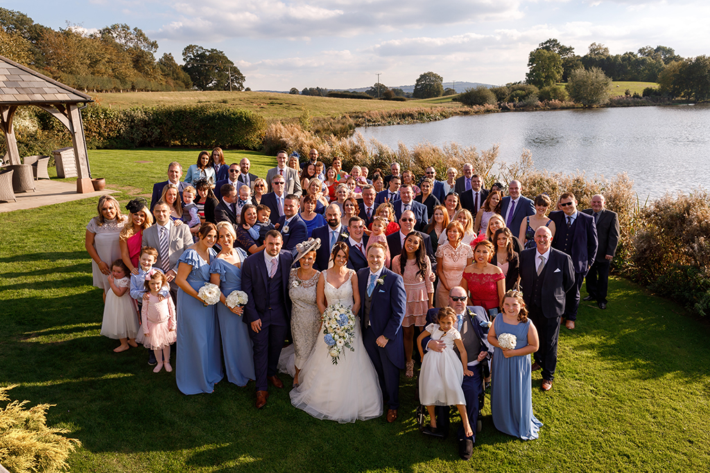 The bride and groom pose for a photo in front of the lake at this barn wedding in Cheshire