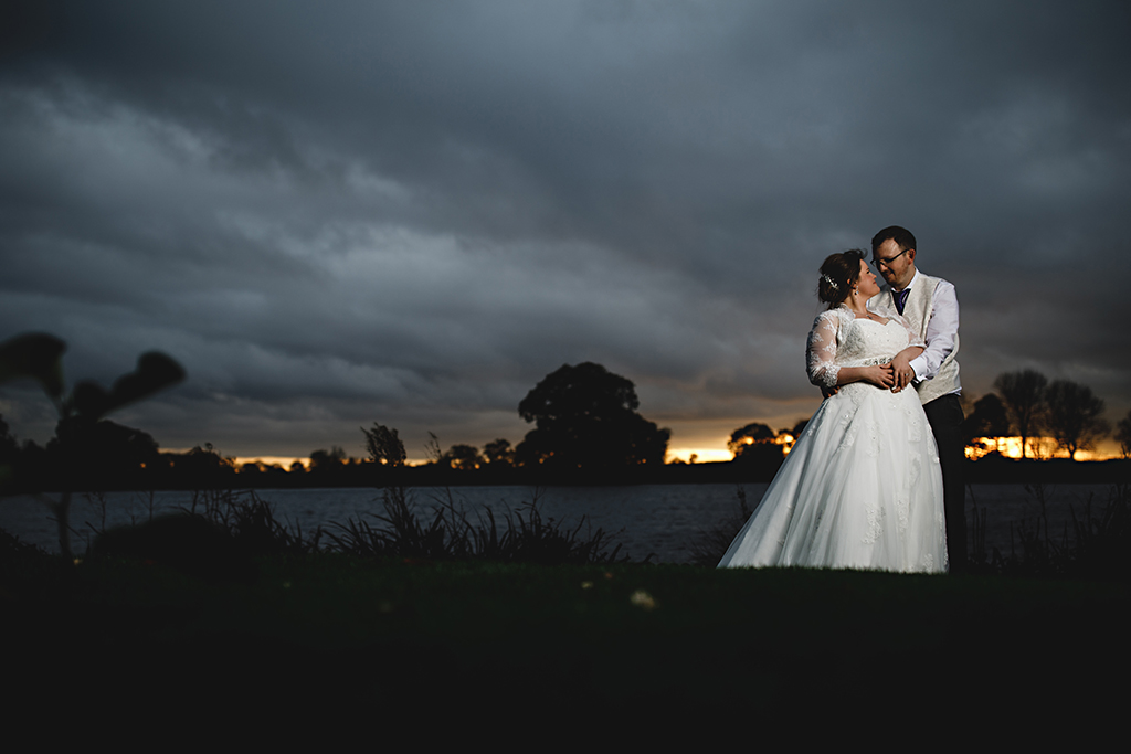 The bride and groom pose for a photo by the lake at this beautiful barn venue in Cheshire
