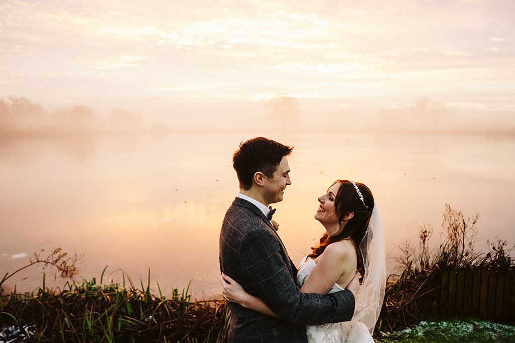 The happy couple pose for a beautiful wedding photo in front of the misty lake